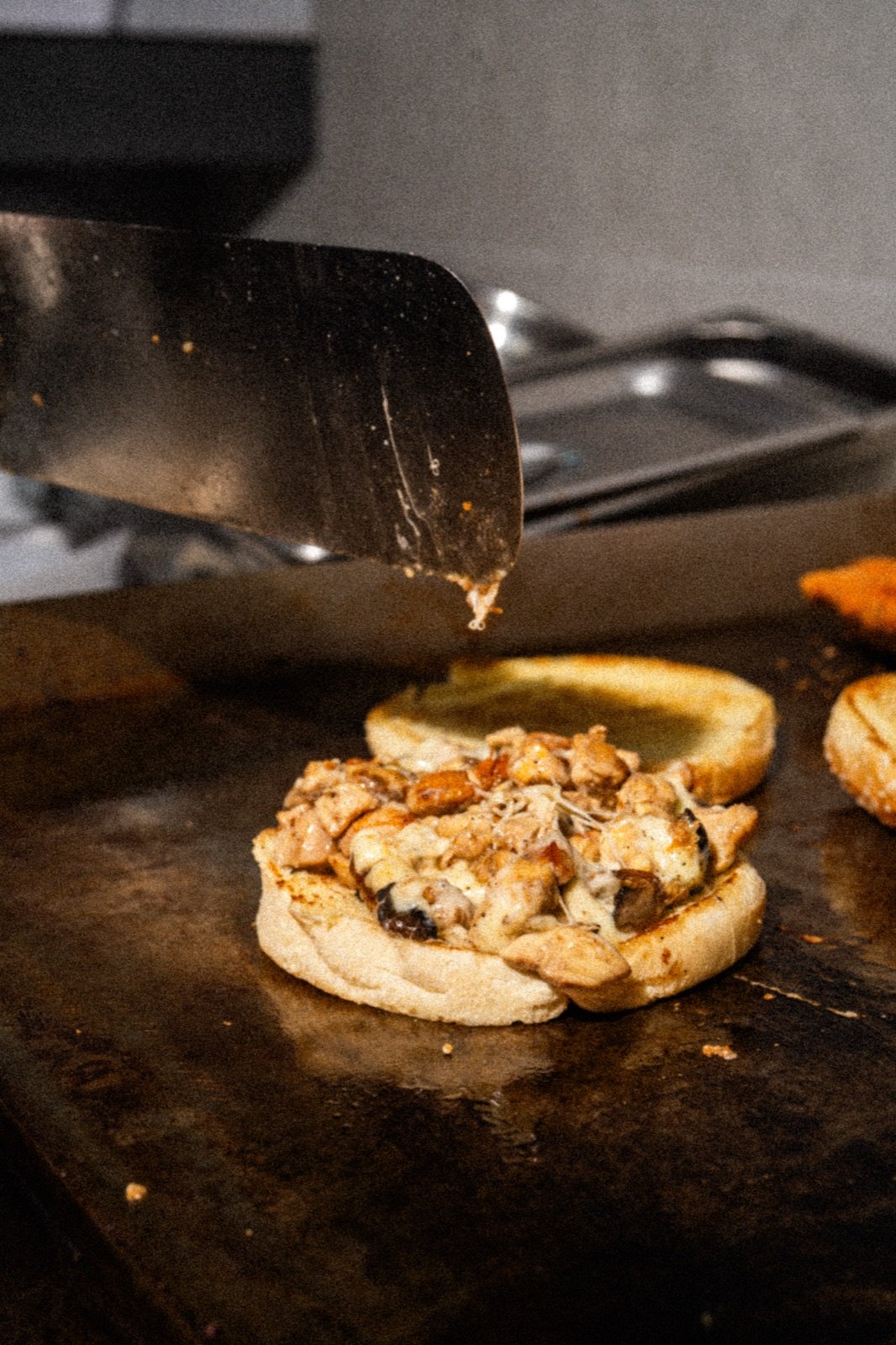 Burger de pollo armándose en la plancha con queso fundido