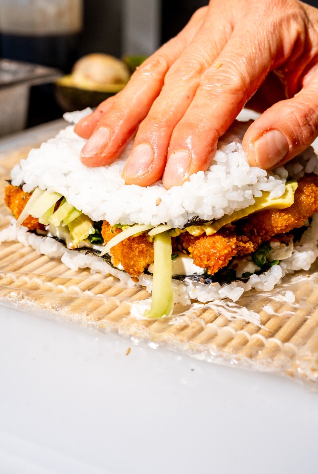 Manos prensando arroz sushi sobre relleno empanizado