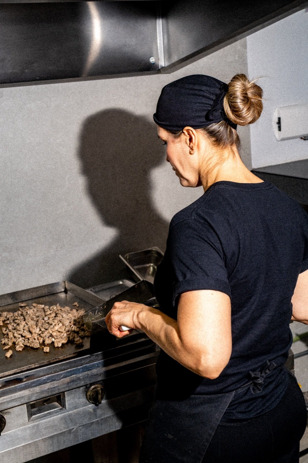 Cocinera de espaldas trabajando la plancha con luz dura