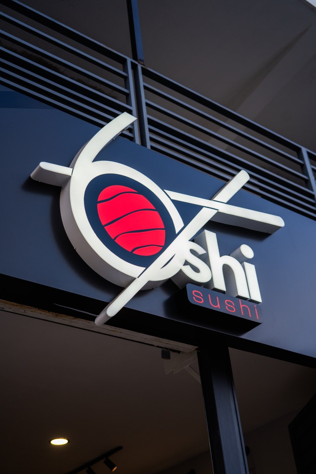 Rótulo iluminado del logo 6shi de noche sobre fachada azul oscuro